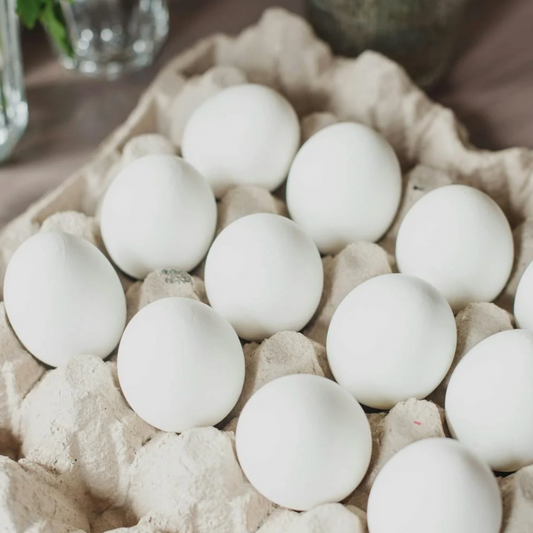 Carton of white eggs on a wooden surface with plants in the background